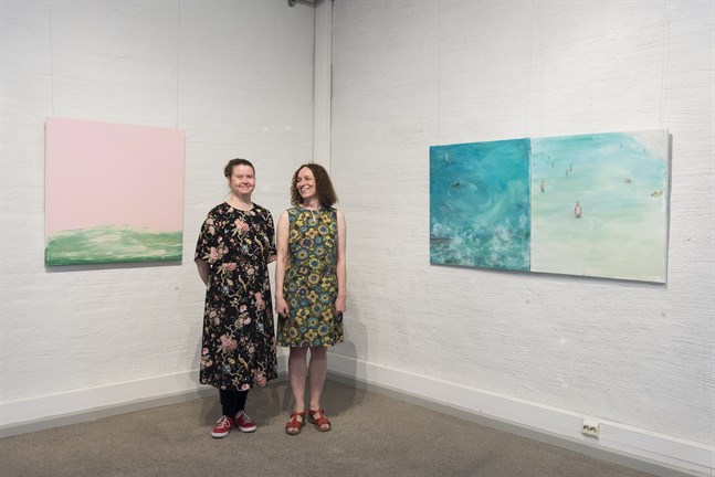 Vännerna Sini-Meri Hedberg och Jaana Valtari ställer ut tillsammans på Tobaksmagasinet i Jakobstad. Till vänster om dem hänger Hedbergs "Movements III", till höger om dem Valtaris "Haj eller delfin" och "Semesterupplevelse".