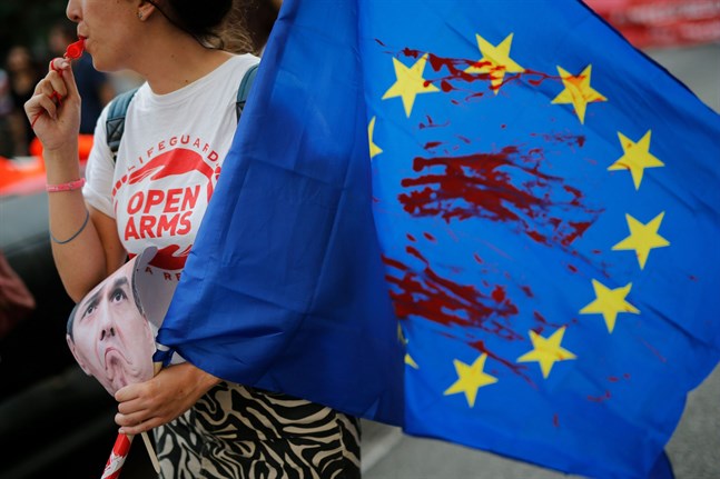 Eftersom rätten till asyl inte är subjektiv borde alla länder inom EU ha samma regler vilket inte är fallet nu, skriver Per Lindeberg om flyktingsituationen i Europa. På bilden håller en demonstrant i en mask som föreställer den spanska premiärministern Pedro Sanchez och en EU-flagga med röd färg som symboliserar blod. Demonstrationen i Barcelona den 13 juli initierades av frivilligorganisationen Proactiva Open Arms, som jobbar med att rädda flyktingar på Medelhavet.