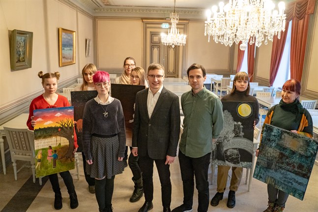 Här är en liten del av det stora gäng som medverkar i "Pictures 2020". Från vänster bildkonsteleverna Sofia Viitanen och Auroora Luoma, celloeleven Eevi Hakala, bildkonstläraren Alli Alho, bildkonsteleven Anni-Maaria Alho, projektledaren Anton Ylikallio, kompositören Christoffer Pörn, bildkonsteleven Ilona Penttinen och konstnären Sirpa Seppelin hållande kollegan Ossi Lehtos målning.