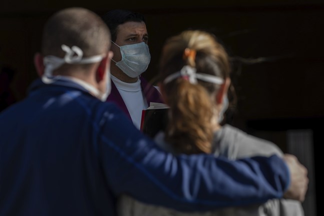 En präst med ansiktsmask håller en begravning i Madrid.
