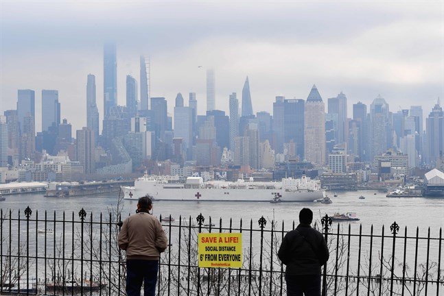 Två personer ser på när fartyget USNS Comfort anländer längs Hudsonfloden i New York på måndagen.