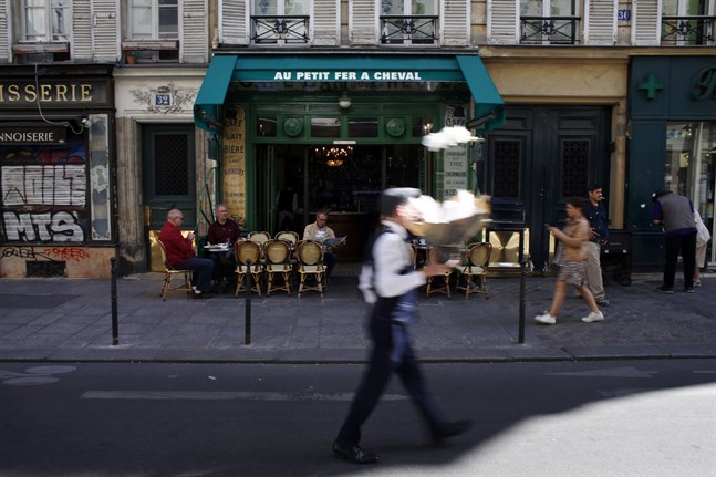 En man passerar med en bukett blommor framför ett café i stadsdelen Marais i Paris. Bild från september 2019.