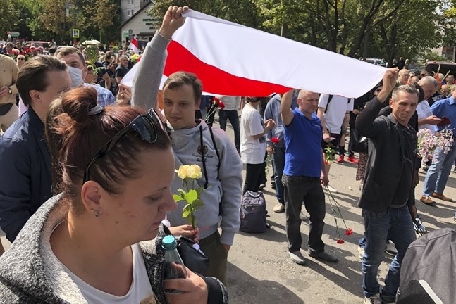 Regimkritiker håller en gammal belarusisk flagga – ofta använd som symbol för oppositionen – i samband med begravningen av en omkommen demonstrant på lördagen.