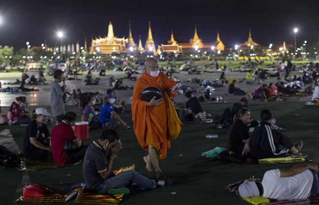 En buddhistmunk delar ut ansiktsmasker till de tusentals demonstranter som vägrade lämna Sanam Luang-torget, utanför det kungliga palatset i Bangkok, under natten till söndag.