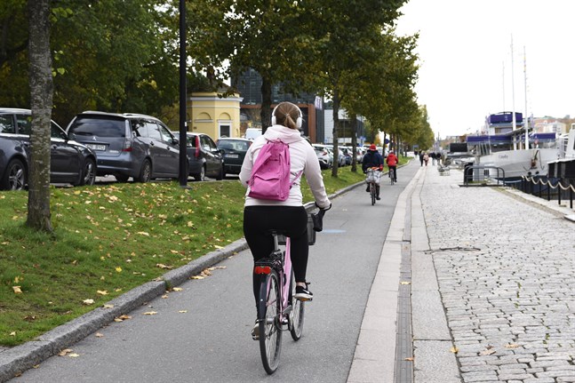 Cyklisterna ska bort från promenadstråket vid Aura å i Åbo och i stället få cykelfiler på Östra Strandgatan (till vänster på bilden). Men på grund av komplicerade trafikarrangemang kommer planeringen av cykelvägen att ta nästa år i anspråk och bygget komma i gång först 2022.