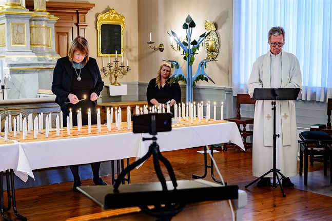 Diakonissan Helena Ekman tänder ljus medan Jockum Krokfors läser upp namnen. Cecilia Åminne i bakgrunden. Parentationen i Jakobstads kyrka är endast virtuell i år.