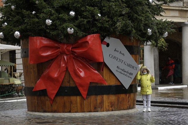 En kvinna med munskydd fotograferas tillsammans med en julgran vid Covent Garden i London i Storbritannien.