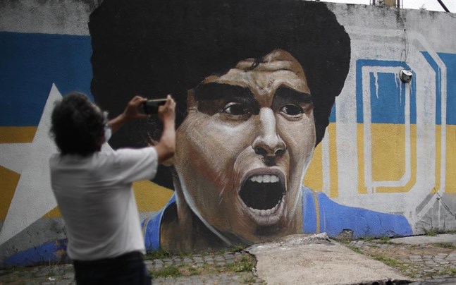 En man tar en bild vid en mur i Buenos Aires med ett gigantiskt Maradona-porträtt.