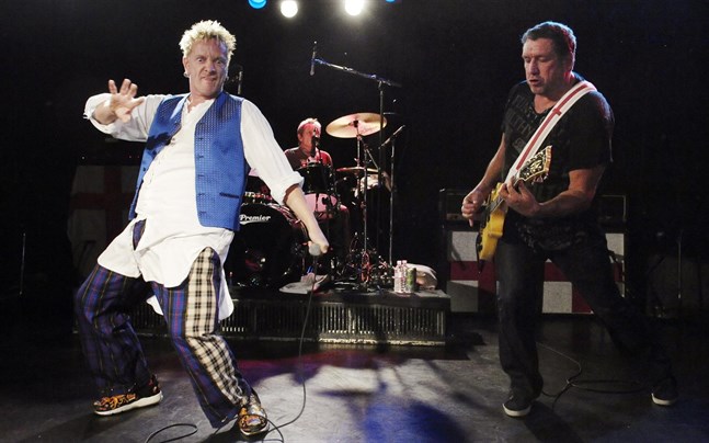Johnny Rotten, med mikrofon i hand, Paul Cook vid trummorna och Steve Jones med gitarr runt halsen vid en Sex Pistols-konsert 2007.
