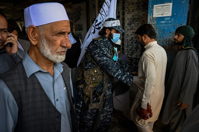 En talibansoldat kroppsvisiterar en man på en marknad i Kabul.
