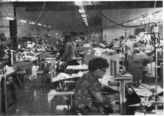 En interiörbild av industrihallen ser ut såhär. Sladdar, maskiner, tygpackor, arbetsbord och -stolar samsas i det stora rummet. Och ändå får ett 40-tal sömmerskor plats bakom högarna av kläder. Men just nu skulle det behövas ytterligare sömmerskor för att man skall nå det uppställda målet.