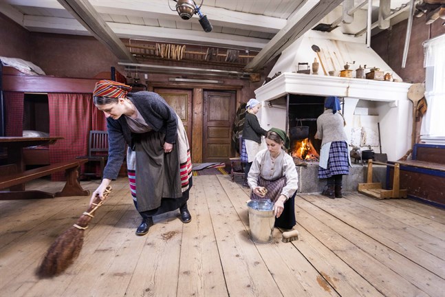 För hundra år sedan gjordes julstädningen med kvast och skurborste. Lotta Ventus som mor Astrid och Anna Moberg som hennes svägerska Signe gör julfint i stugan i kalendern "Tidernas jul".