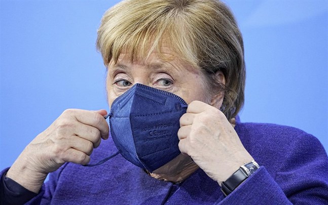 Angela Merkel tar på sig munskyddet inför en presskonferens om nya restriktioner i Tyskland.
