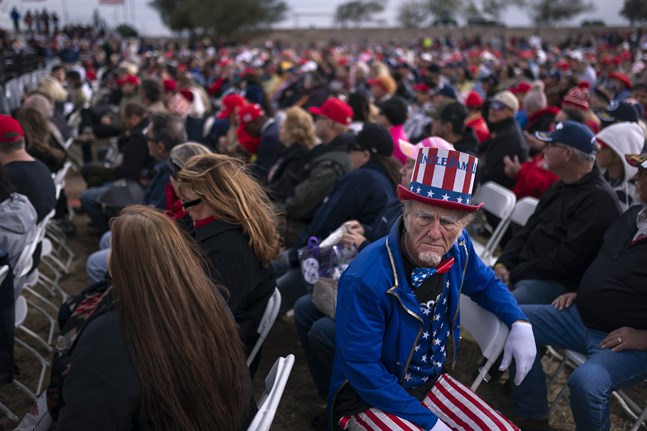 En Trump-anhängare utklädd till Uncle Sam lyssnar medan olika talare värmer upp scenen inför ex-presidentens framträdande.