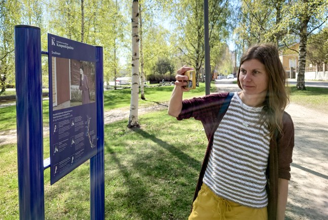 Rosanna Telaranta demonsterar hur bilden på skylten startar en video i mobilen. Karleby nationalstadspark har fått guideskyltar med förstärkt verklighet.