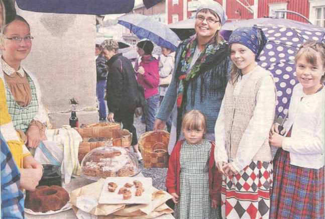 Familjen Norrvik trotsade regnet på gammaldagstorgdagen på lördagen i Kristinestad och tog möjligen hem priset som stiligast klädda familjen på torget på lördagen. Här köper mamma Åsa Norrvik, minstingen Sara Norrvik, Anna Norrvik och Moa Norrvik hembakt av Adelina Appel, längst till vänster på bild.