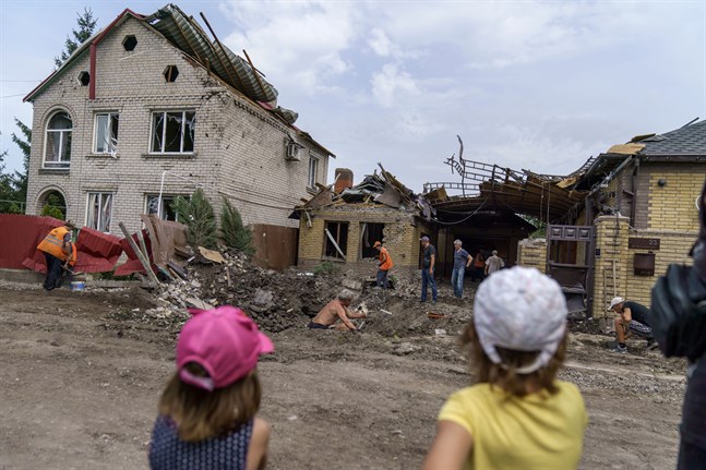 Två barn tittar på medan hjälparbetare städar upp efter ett bombnedslag i Kramatorsk i Donetsk. Bilden är tagen 12 augusti.