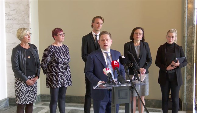 Markus Lohi berättar om social- och hälsovårdsutskottets beslut. Bakom honom står Veronica Rehn-Kivi (SFP), Merja Kyllönen (VF), Ilmari Nurminen (SDP), Mia Laiho (Saml) och Sofia Virta (Grön).